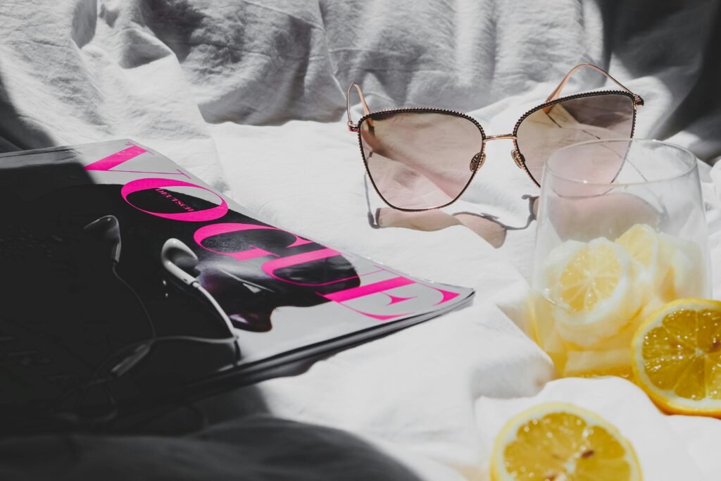 A chic summer setup featuring sunglasses, a fashion magazine, and a refreshing lemon drink.